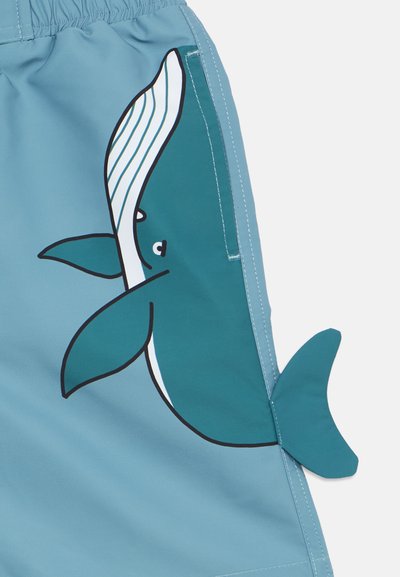 Μαγιό σορτς σε ανοιχτό μπλε ύφασμα με γραφικό φάλαινας σε τιρκουάζ, με καμπυλωτές γραμμές και λεπτομέρεια πτερυγίου, που αναδεικνύουν παιχνιδιάρικα, υδάτινα σχέδια.