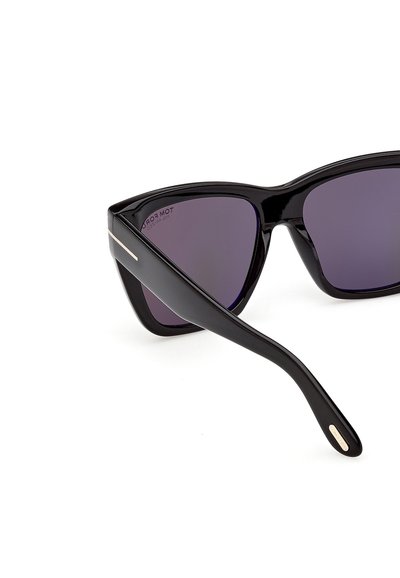 Lunettes de soleil noires à monture œil de chat avec des verres foncés, présentant un détail métallique subtil aux extrémités des branches, présentées sur un fond blanc.
