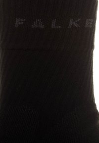Calcetines negros de tela texturizada con diseño acanalado, que presentan una sutil marca "FALKE" impresa en gris en la parte superior.
