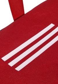 Bolsa de tela roja con tres franjas horizontales blancas y una correa roja resistente, que muestra un material texturizado y duradero.