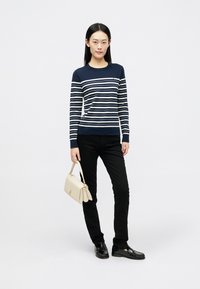 Sweater às riscas navy com linhas creme, jeans skinny pretos e uma mala bege. Sapatos pretos completam o look. Detalhes em metal minimais.