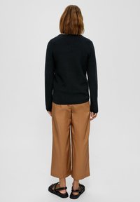 Zwarte gebreide trui met lange mouwen, gecombineerd met bruine wijde broek en zwarte sandalen. Uitzicht van achteren, die de silhouet van de outfit toont.
