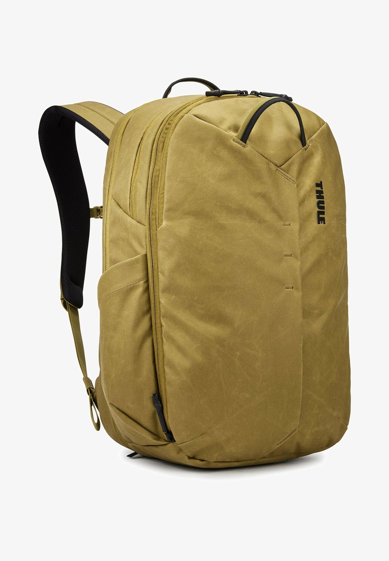 Mochila caqui con una tela texturizada, que cuenta con un compartimento principal con cremallera, correas de hombro acolchadas y un bolsillo lateral para accesorios.