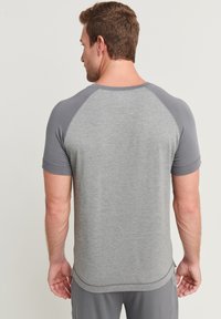 Grå sport-t-shirt med korta raglanärmar. Mjuk, slät textur, med en rundad halsringning och subtil sömnadsdetalj vid fållen.