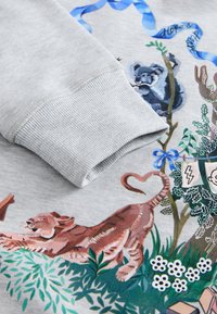 Hall hallipluus, millel on soonikuga mansett, kaunistatud värvikate loomade illustratsioonide, taimede ja erinevate kujudega, sealhulgas südame ja vurrudega.