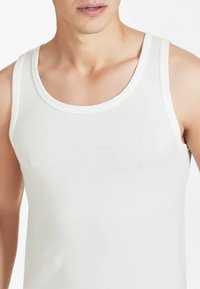 Canottiera bianca in cotone con scollatura arrotondata e spalline larghe, caratterizzata da una texture morbida e un design aderente.