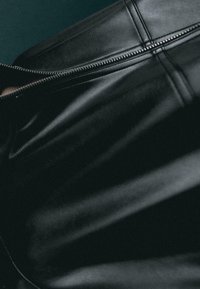 Lähikuva mustasta nahkavaatteesta, jossa näkyy hopeinen vetoketju ja yksityiskohtaiset ompeleet sauman varrella.