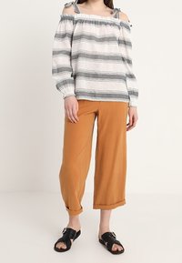 Vit off-shoulder-blus med svarta horisontella ränder, kombinerad med orange vida byxor. Bärs med svarta slidesandaler.