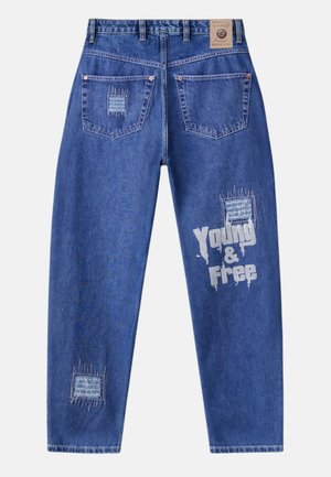 Blue denim jeans with two back pockets, distressed patches, and white text "Young & Free" on the right leg. Leather label on the waistband.