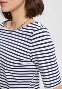 Top de rayas azul marino y blanco de manga corta con escote barco, hecho de una tela suave, con una textura lisa y un diseño minimalista.