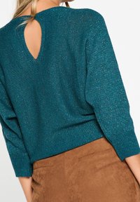 Teal stickad tröja med en texturerad finish, med en nyckelhålskärning i ryggen och trekvartslånga ärmar. Matchad med en brun fuskmocka kjol.