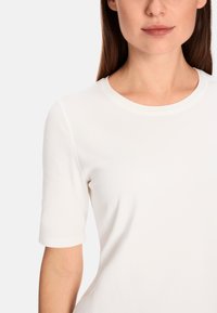 White short-sleeve top, round neck, smooth texture, slightly fitted design, simple and clean appearance without patterns or accents.