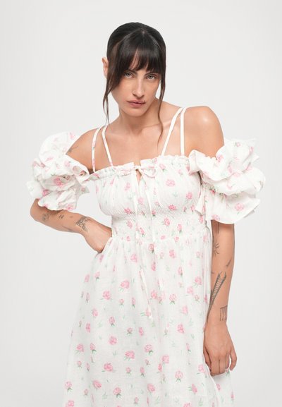 Hvid off-the-shoulder kjole med pufærmer, blomsterprint i rosa og grøn, smocket liv og en frontbinding.