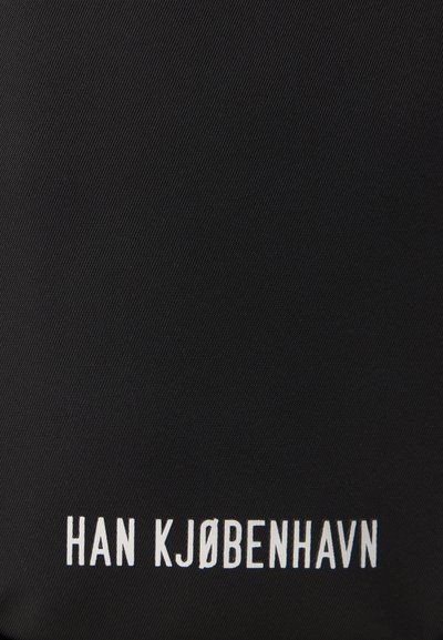 Black fabric surface featuring white text reading "HAN KJØBENHAVN." Material has a textured finish with a woven pattern.