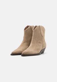 Cizme cowboy din suede bej, cu vârfuri ascuțite, toc înclinat și cusături decorative pe laterale. Textură netedă cu un design clasic.