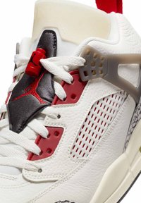 Hvide lædersneakers med røde og sorte detaljer, der har perforerede detaljer, hvide snørebånd og en grå plastik støtte på siden.