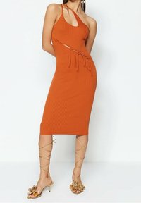 Robe midi orange à côtes avec décolleté asymétrique et découpes sur les côtés, associée à des sandales dorées à lanières ornées de fleurs.