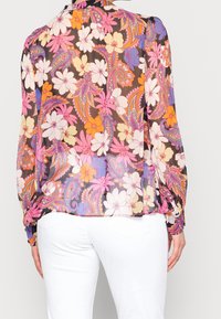 Blouse fleurie avec manches longues bouffantes en tissu transparent. Présente un motif cachemire coloré avec des fleurs blanches et roses sur fond noir.