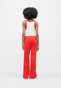 Czerwone spodnie sportowe z białymi paskami po bokach i rozcięciami u dołów, zestawione z bezrękawnym białym topem z czerwonym kołnierzykiem.