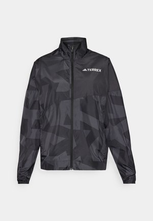 Veste légère noire avec un col haut, fermeture éclair et motif géométrique. Présente le logo "TERREX" en blanc sur le côté supérieur gauche.