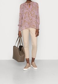 Blusa a fiori in marrone chiaro e viola, pantaloni slim-fit crema, sneaker beige con suola bianca e una grande borsa tote taupe.