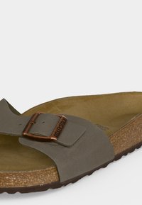 Καφέ σανδάλι Birkenstock με έναν ιμάντα, ρυθμιζόμενο χάλκινο αγκράφα και πάτο φελλού σε λευκό φόντο.