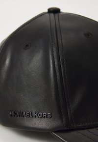 Căciulă din piele neagră, cu o textură netedă, vizor curbat și logo-ul embosat "MICHAEL KORS" pe partea stângă frontală.