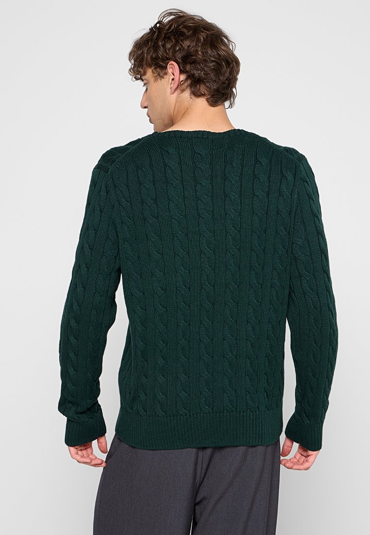 Suéter verde de punto con un patrón de trenzas, cuello redondo y dobladillo y puños acanalados, con un ajuste relajado y superficie texturada.