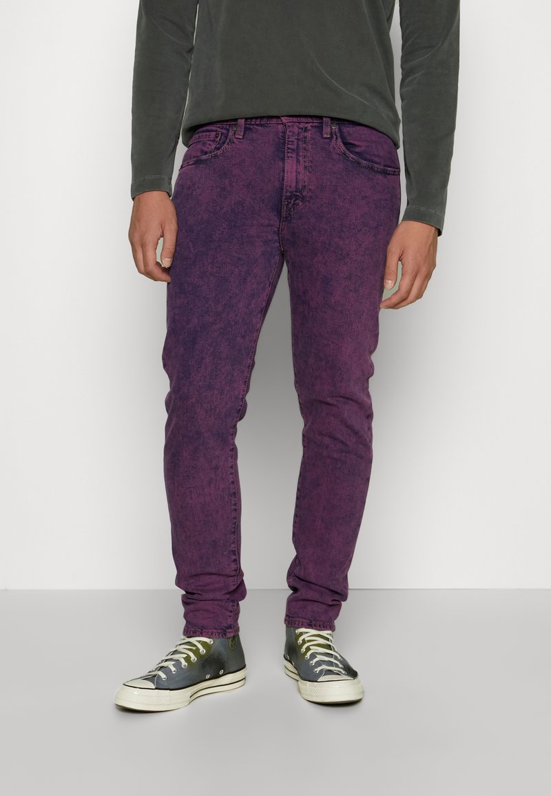 Jeans de mezclilla morados con un acabado texturizado, cinco bolsillos y un corte ajustado, combinados con zapatillas gris y blancas con acentos metálicos.