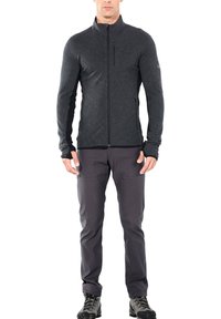 Giacca aderente con zip di colore grigio scuro, in tessuto testurizzato con colletto alto e aperture per il pollice, abbinata a pantaloni grigi scuri e scarponi da trekking neri.