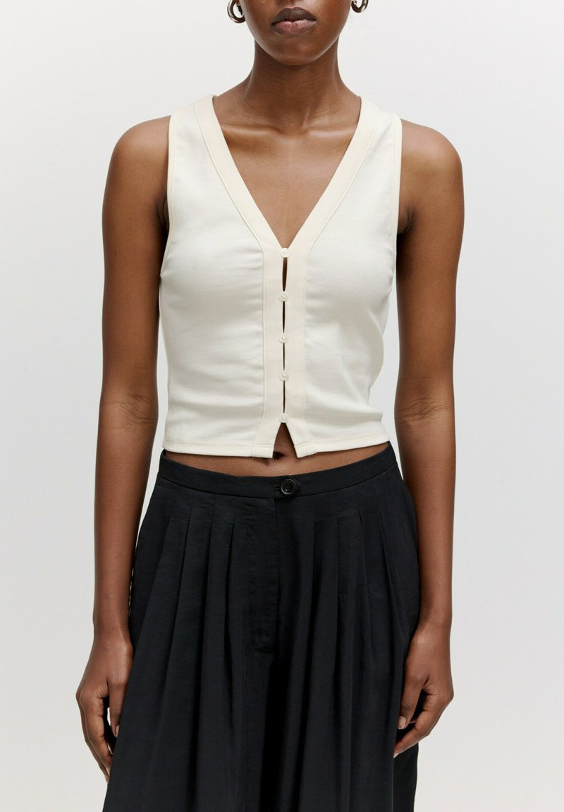 Off-white ärmelloses Oberteil mit tiefem V-Ausschnitt, das eine Vorderknopfleiste und einen verkürzten Saum hat. Weicher Stoff mit leichtem Stretch.