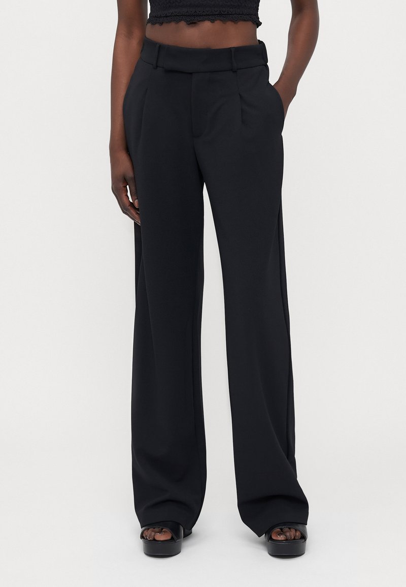 Black wide-leg trousers with a smooth texture, featuring front pleats and a tailored waistband. Worn with a cropped top and platform sandals.