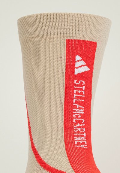 Calcetín de punto beige con un diseño gráfico audaz en rojo y blanco, con texto y acentos triangulares a lo largo del costado.