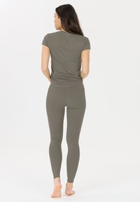 Olivenfarbene Sportbekleidungsreihe bestehend aus einem kurzärmeligen Oberteil und enganliegenden Leggings mit gerippten Akzenten. Glatte Textur, minimalistisches Design.