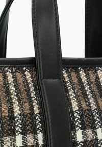 Sac tissé avec des bordures en cuir noir, présentant un motif de rayures horizontales marron et crème, mettant en valeur la texture et le détail.