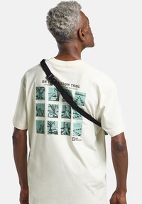 T-shirt oversize di colore crema con un design grafico composto da nove pannelli illustrati in verde e la scritta "SULLA VIA DELLA LIBERTÀ" sopra.