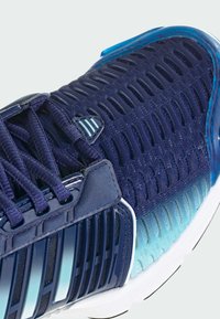 Lähikuva laivastonsinisestä ja sinisävyisestä urheilukengästä, jossa on verkkopäällinen, vahvistettu nauhanpidike ja ilmastoitu muotoilu.