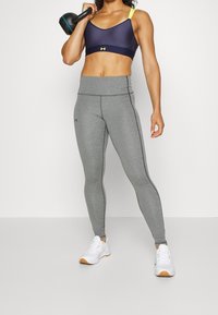 Szare legginsy fitness z gładką teksturą i czarnymi bocznymi szwami, w połączeniu z granatowym biustonoszem sportowym z neonowymi żółtymi akcentami.