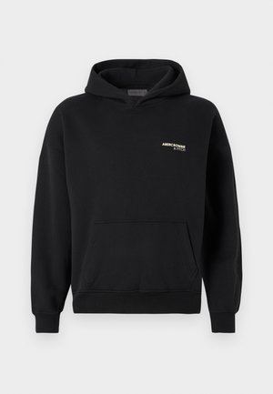 Zwarte hoodie met een frontzak, voorzien van een klein gouden logo op de linkerkant van de borst. Gemaakt van zacht materiaal met een ontspannen pasvorm en geribde manchetten.