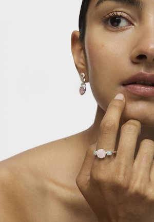 Anillo de cuarzo rosa con acentos verdes sobre una banda de plata, acompañado de pendientes colgantes con piedras rosas a juego. Diseño simple y elegante.