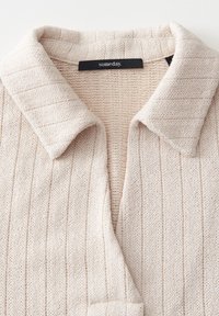 Helle beigefarbene Strickjacke mit Kragen und vertikaler Rippstruktur. Hergestellt aus weichem Strickmaterial, versehen mit einem Etikett mit dem Markennamen "someday."