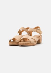 Beige suède sandalen met hakken, met kruislings banden, verstelbare gespsluiting en een blokhak met kurkstructuur. Zacht interieur voor comfort.
