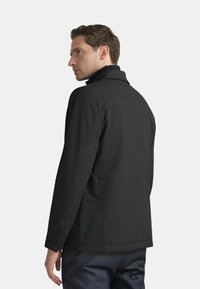 Giacca softshell nera con colletto alto, design snodato e dettagli di cucitura visibili. Presenta una vestibilità comoda e linee pulite.