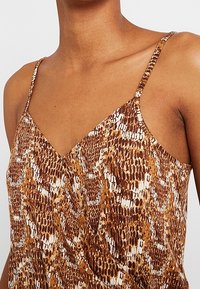 Bruin en beige slangenprint spaghetti bandtop met een V-hals. Glad, lichtgewicht stof met een subtiele glans en verstelbare bandjes.