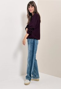 Maglia a maniche lunghe di un viola scuro abbinata a jeans a gamba larga azzurri con una striscia laterale blu scuro, styled con sneakers color crema.