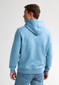 Sudadera azul claro hecha de un tejido suave, con capucha con cordón, puños y dobladillo acanalados, y un diseño de espalda sin costuras. Combinada con vaqueros.