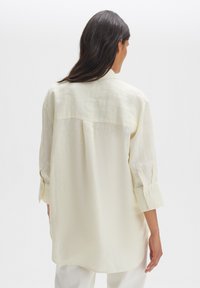 Light yellow linen shirt with a loose fit, collared neckline, and three-quarter sleeves. Subtle texture and back yoke detail.