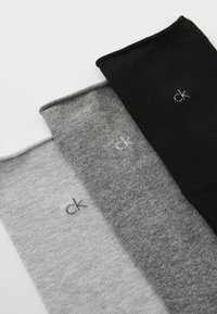 Tri para nogavic v svetlo sivi, temno sivi in črni barvi, izdelane iz mehkega materiala, vsaka z majhnim logotipom "ck".