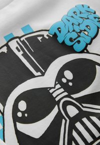 Biała bluza z grafiką czarnego hełmu oraz napisem "DARK SIDE" w niebieskiej, zabawnej czcionce. Gładka tekstura z wyrazistymi kontrastami.