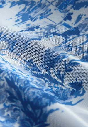 Blau-weiß gemusteter Stoff mit strukturierter Oberfläche, der abstrakte Blumen- und Blattmotive auf einem texturierten Hintergrund zeigt.